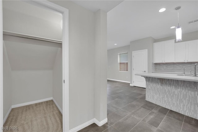 kitchen featuring hanging light fixtures, backsplash, light countertops, white cabinets, and baseboards