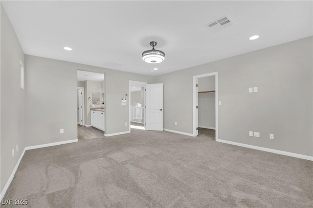 unfurnished bedroom with visible vents, a walk in closet, connected bathroom, carpet flooring, and baseboards