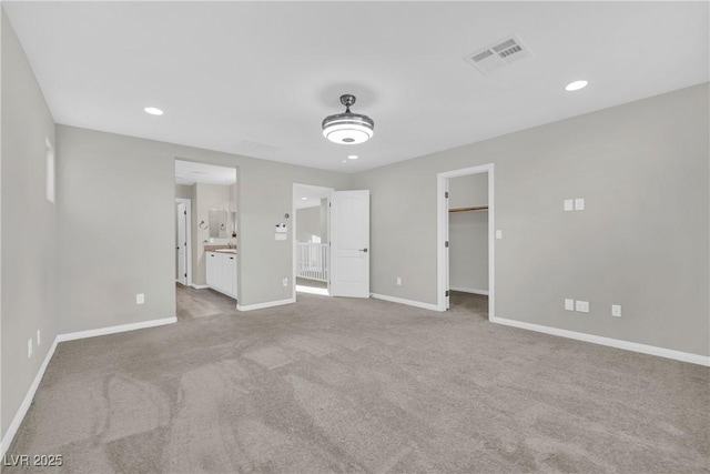 unfurnished bedroom with a walk in closet, visible vents, carpet flooring, and baseboards