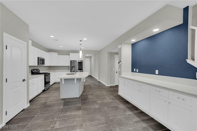 kitchen with white cabinets, stainless steel appliances, a kitchen island with sink, light countertops, and decorative light fixtures