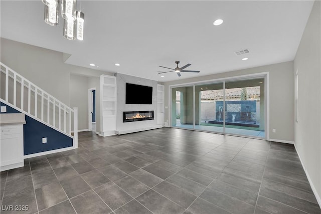 unfurnished living room with visible vents, baseboards, stairway, recessed lighting, and ceiling fan with notable chandelier