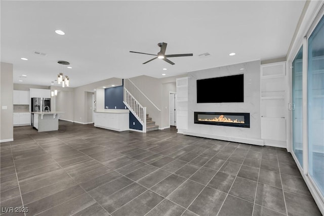 unfurnished living room featuring baseboards, stairway, recessed lighting, a glass covered fireplace, and a ceiling fan