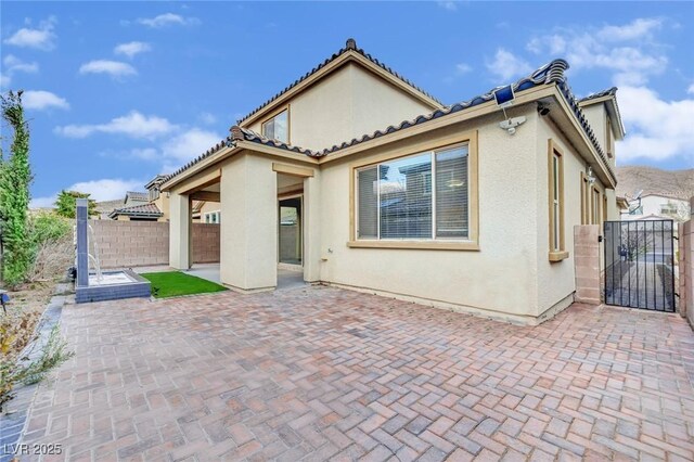 rear view of property featuring a gate, stucco siding, fence, and a patio area