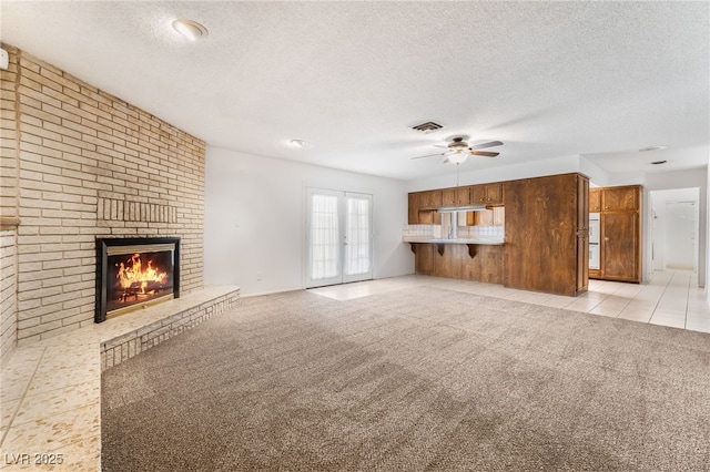 unfurnished living room with a brick fireplace, light colored carpet, a textured ceiling, and ceiling fan