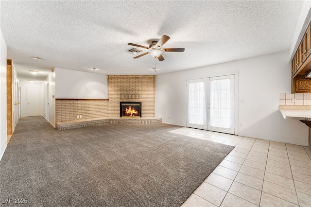 unfurnished living room featuring a fireplace, light colored carpet, ceiling fan, a textured ceiling, and french doors