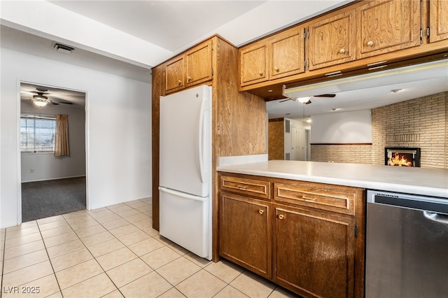 kitchen featuring light tile patterned flooring, stainless steel dishwasher, white fridge, ceiling fan, and a fireplace