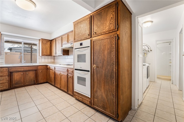 kitchen featuring washer and dryer, double oven, sink, decorative backsplash, and light tile patterned floors