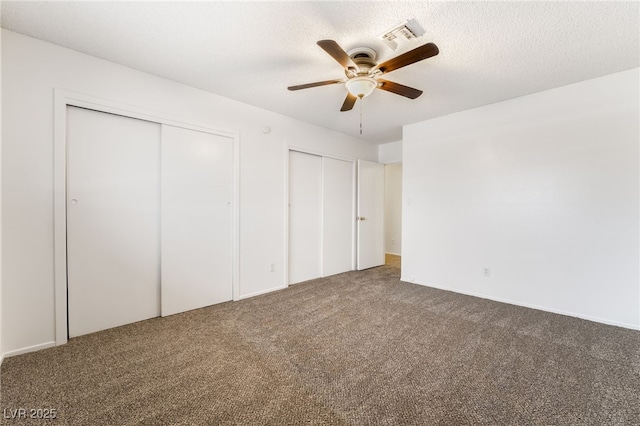 unfurnished bedroom featuring ceiling fan, two closets, a textured ceiling, and carpet