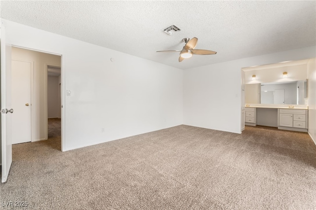 unfurnished bedroom with carpet, built in desk, a textured ceiling, and ensuite bath