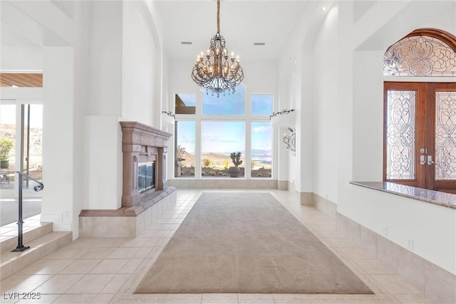 unfurnished living room with a tile fireplace, a towering ceiling, light tile patterned floors, and a chandelier