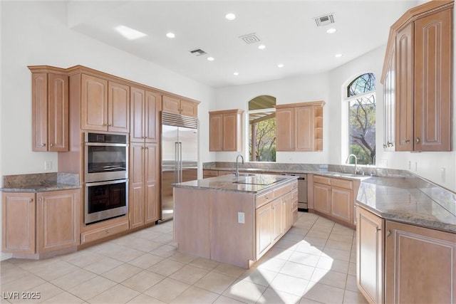 kitchen with light tile patterned floors, stainless steel appliances, an island with sink, and stone counters