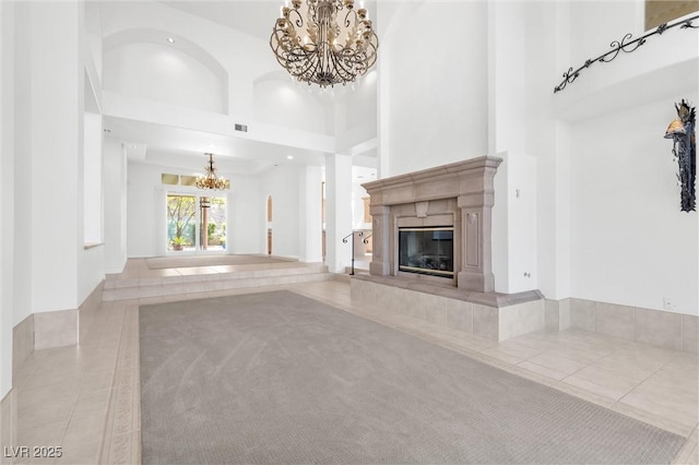 unfurnished living room with an inviting chandelier, light tile patterned floors, a fireplace, and a high ceiling