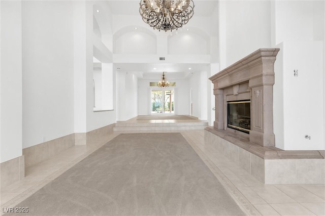 unfurnished living room with a high ceiling, a tile fireplace, light tile patterned flooring, and an inviting chandelier