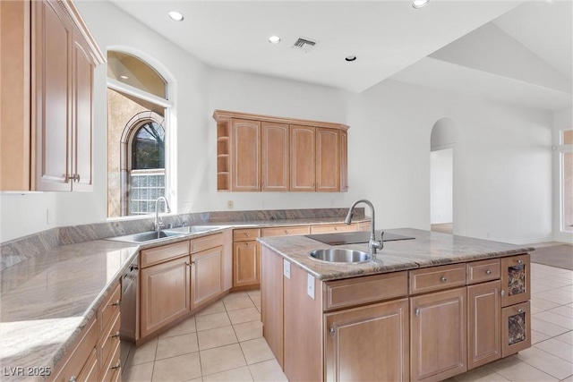 kitchen with light stone counters, sink, light tile patterned floors, and an island with sink