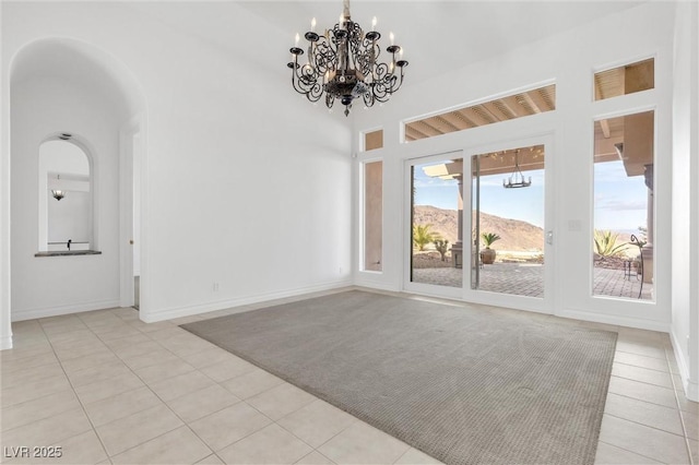 spare room with light tile patterned flooring, a mountain view, a towering ceiling, and an inviting chandelier