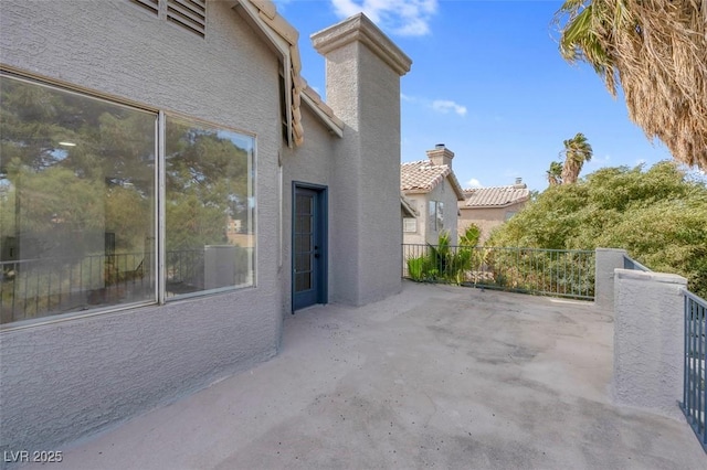 exterior space featuring stucco siding, a tiled roof, a chimney, and a patio