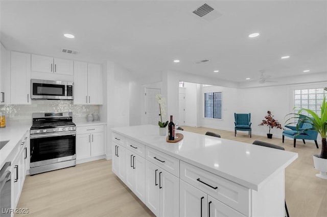 kitchen with a center island, light hardwood / wood-style flooring, stainless steel appliances, decorative backsplash, and white cabinets