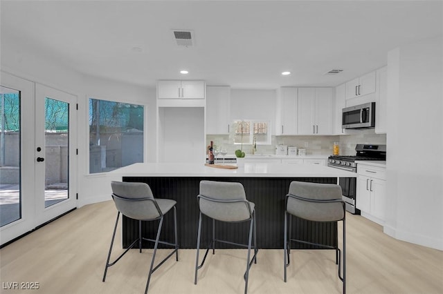 kitchen with white cabinetry, stainless steel appliances, a center island, and light wood-type flooring