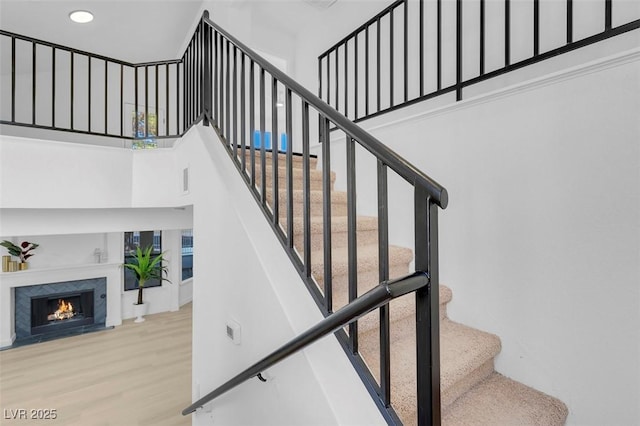 stairway with a towering ceiling, hardwood / wood-style floors, and a high end fireplace