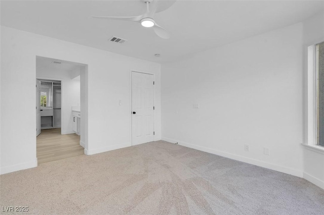 unfurnished bedroom featuring ceiling fan, light colored carpet, and ensuite bath