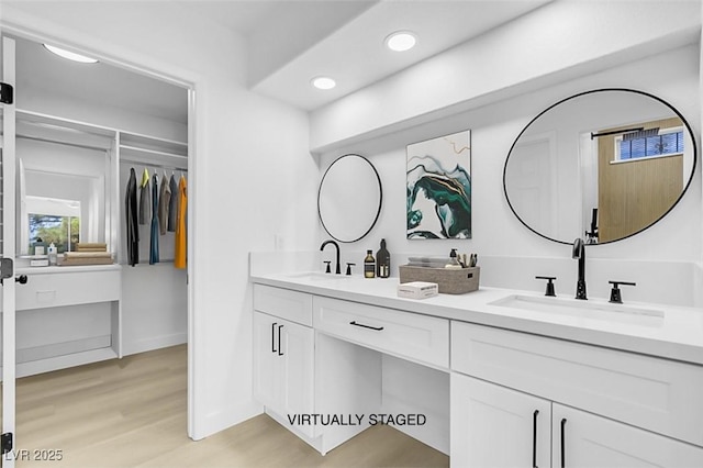 bathroom featuring wood finished floors, a sink, double vanity, and recessed lighting