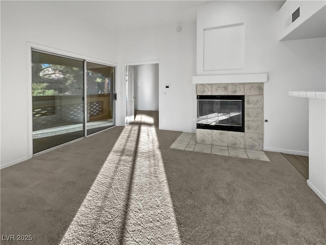 unfurnished living room featuring a tile fireplace, a towering ceiling, and dark carpet