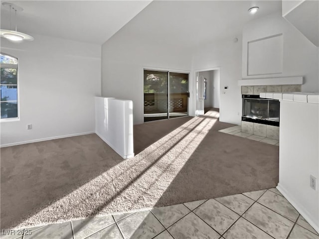 unfurnished living room featuring a tiled fireplace, light colored carpet, and high vaulted ceiling