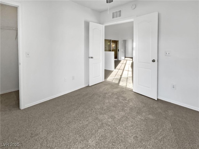 unfurnished bedroom with dark colored carpet, a walk in closet, and a closet