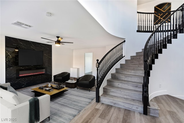 living room with a high end fireplace, wood-type flooring, and ceiling fan