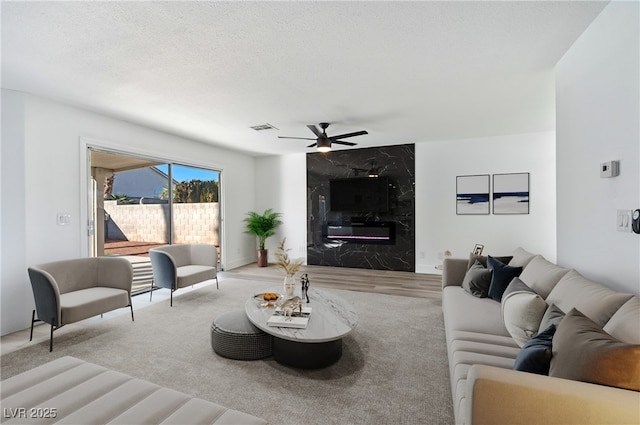 living room featuring ceiling fan, a high end fireplace, and a textured ceiling