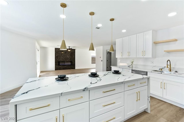 kitchen featuring white cabinetry, hanging light fixtures, sink, and light stone counters