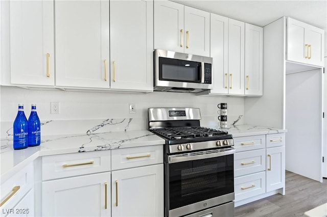 kitchen with light stone countertops, light hardwood / wood-style floors, white cabinets, and appliances with stainless steel finishes