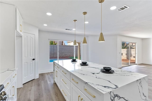 kitchen with a kitchen island, pendant lighting, white cabinets, and light stone counters