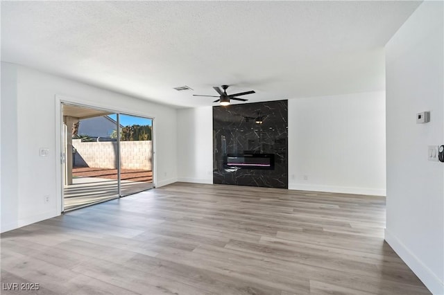 unfurnished living room featuring a high end fireplace, a textured ceiling, and light wood-type flooring