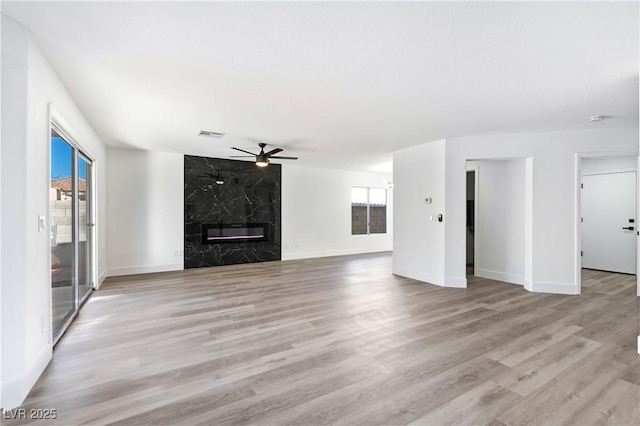 unfurnished living room featuring plenty of natural light, light hardwood / wood-style floors, a premium fireplace, and ceiling fan