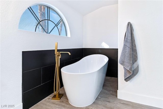 bathroom featuring wood-type flooring, a bath, vaulted ceiling, and tile walls