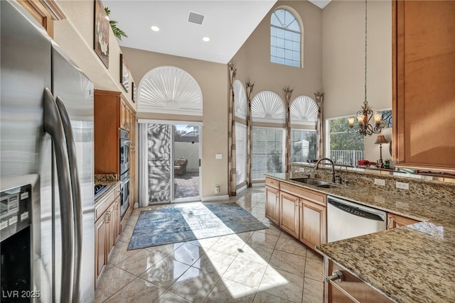 kitchen with hanging light fixtures, stainless steel appliances, light stone counters, a towering ceiling, and sink