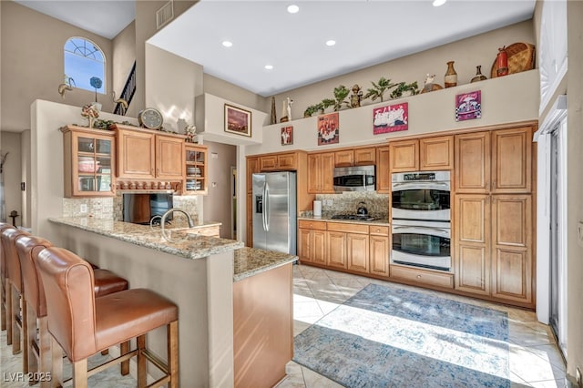 kitchen with kitchen peninsula, stainless steel appliances, backsplash, light stone counters, and a breakfast bar area