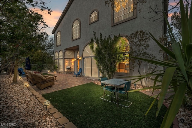 back house at dusk featuring a patio and a yard