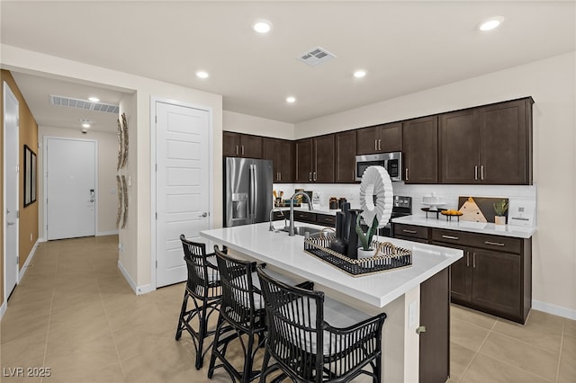 kitchen with a breakfast bar, sink, tasteful backsplash, a center island with sink, and appliances with stainless steel finishes