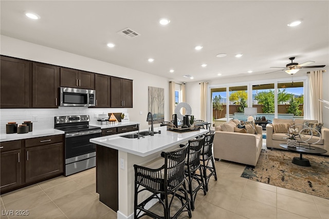 kitchen with an island with sink, sink, backsplash, a kitchen bar, and stainless steel appliances