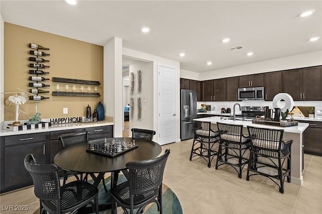 kitchen featuring dark brown cabinetry, a breakfast bar area, a center island with sink, stainless steel appliances, and backsplash