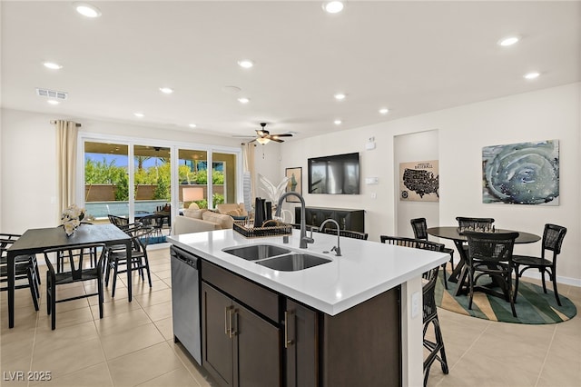 kitchen featuring sink, a kitchen island with sink, dark brown cabinets, light tile patterned flooring, and stainless steel dishwasher