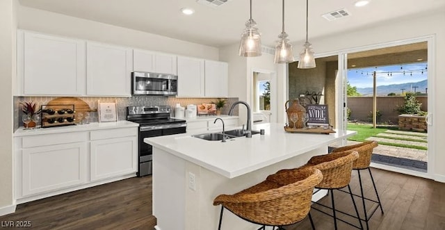 kitchen featuring appliances with stainless steel finishes, decorative light fixtures, sink, white cabinets, and a center island with sink