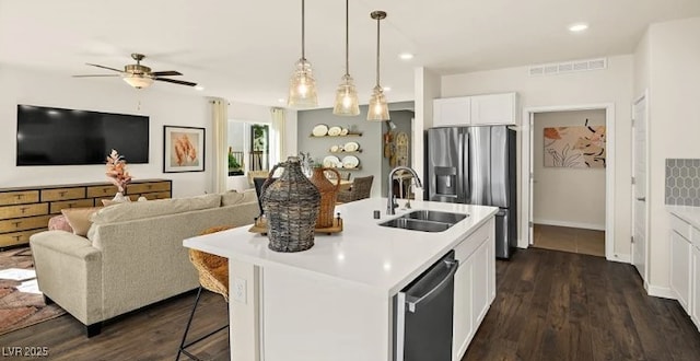 kitchen featuring decorative light fixtures, white cabinetry, sink, stainless steel appliances, and a center island with sink