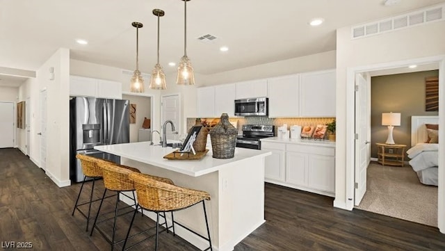 kitchen with a breakfast bar, a kitchen island with sink, stainless steel appliances, white cabinets, and decorative light fixtures