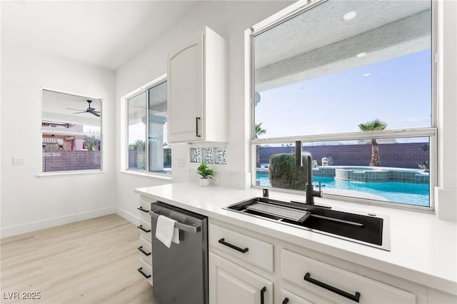 kitchen with white cabinetry, a sink, light countertops, light wood-style floors, and dishwasher