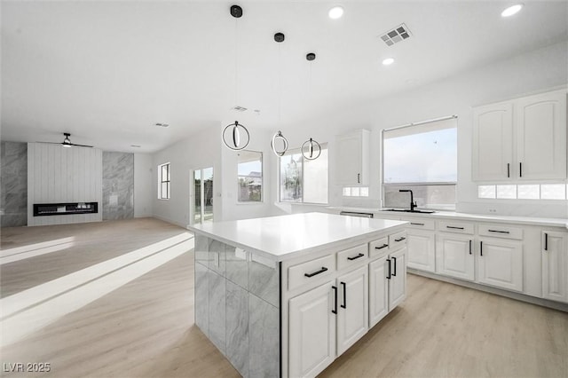 kitchen featuring a kitchen island, pendant lighting, a large fireplace, sink, and white cabinets