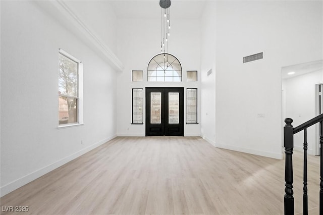 entryway with french doors, a towering ceiling, and light wood-type flooring