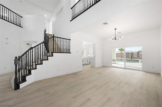 unfurnished living room featuring a towering ceiling, a chandelier, and light hardwood / wood-style floors